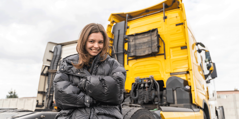 Young female truck driver standing at the back of her semi-truck.